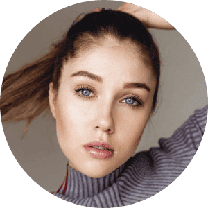 Person with light brown hair pulled back, wearing a grey sweater, looks directly at the camera.